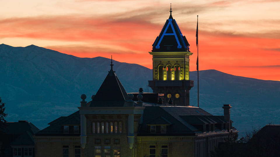 Utah State University's Old Main lit in yellow and blue lights.
