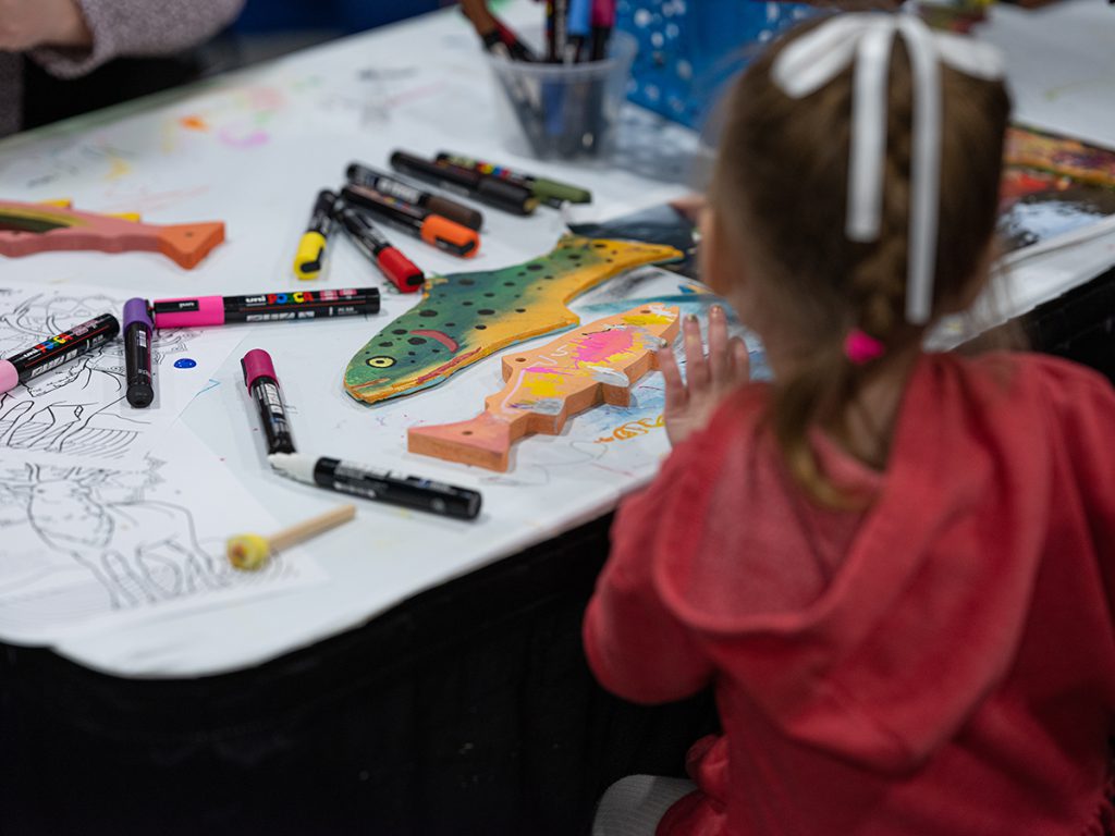 A young girl is painting a wooden fish.