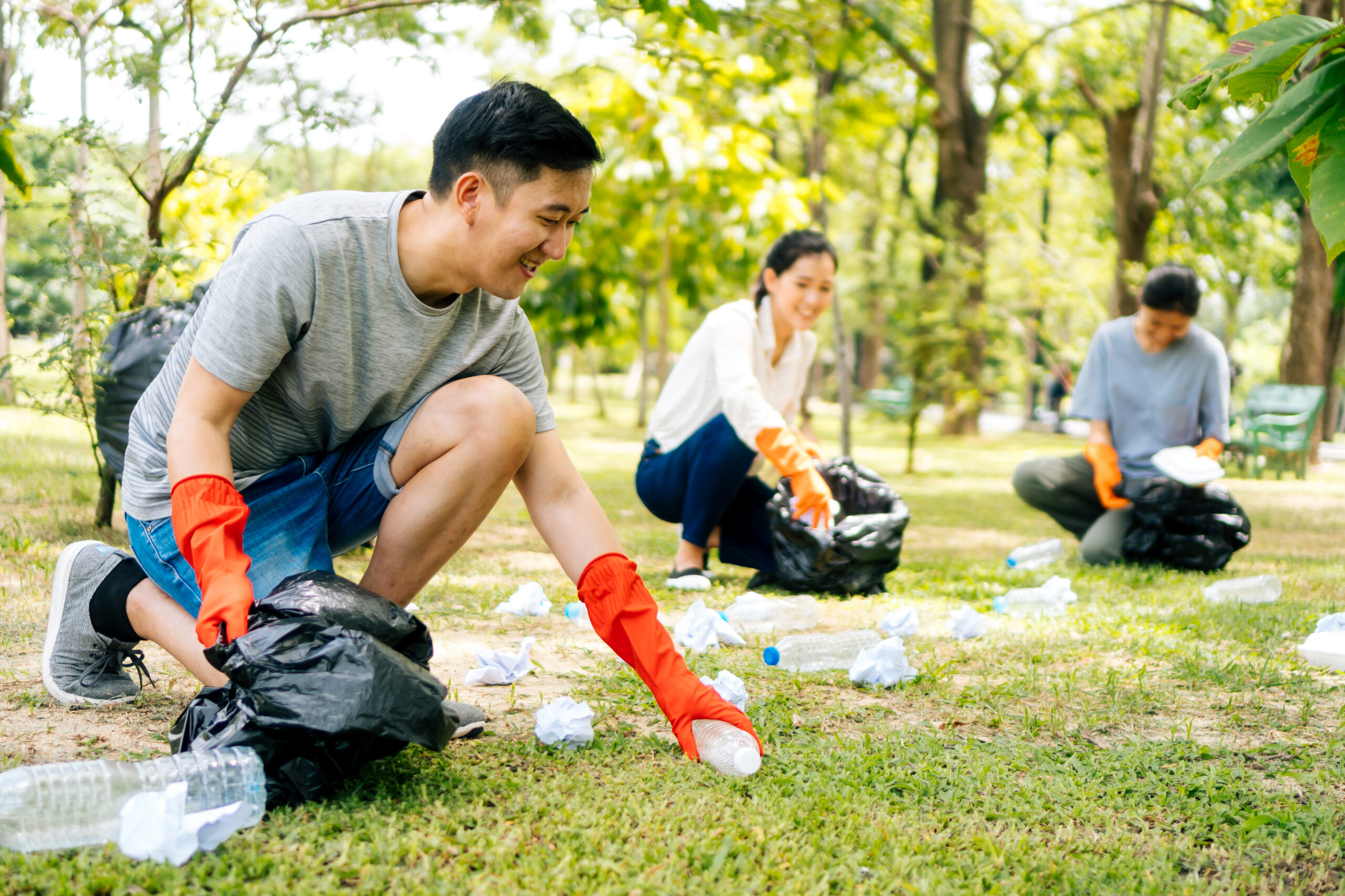 Three volunteers wearing orange rubber gloves picking up litter as part of America’s youth.